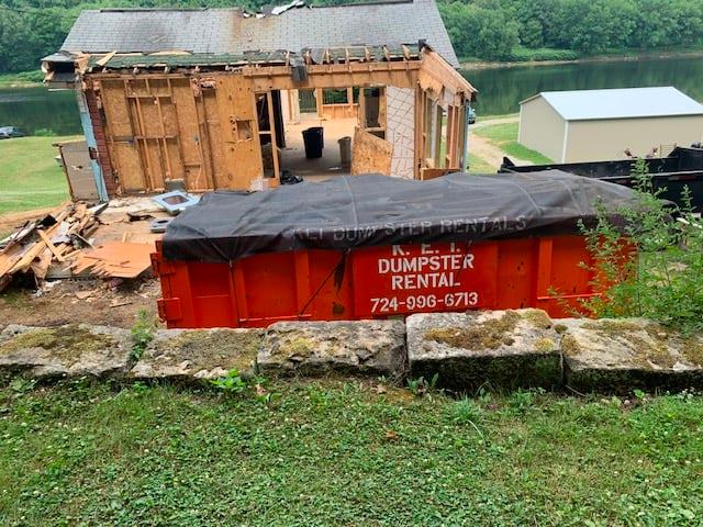 A KEI roll-off dumpster sits behind a house that's being demolished because of fire damage. 