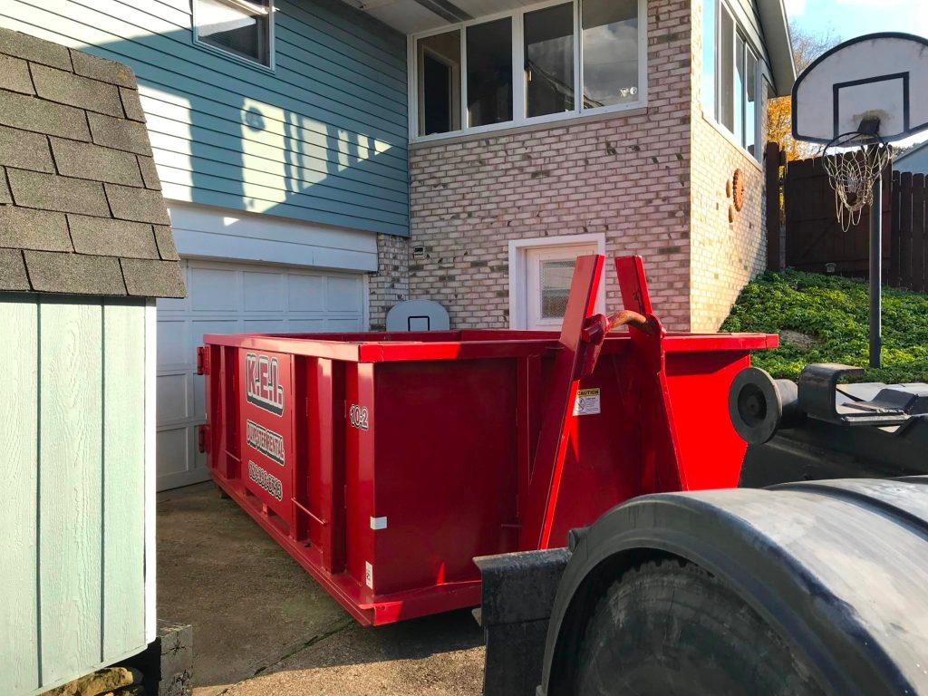 Dumpster rental services company KEI delivers a roll-off dumpster to a customer and leaves it in their driveway. 