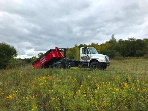 A KEI dumpster rental services truck drops off a rental dumpster in a field where a client requested delivery.