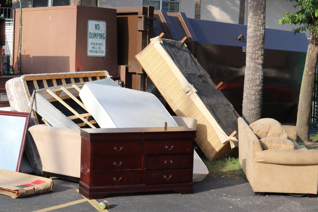 Large items like a dresser, mattresses, a couch, and bedframe lay on the street waiting to be loaded into a roll-off dumpster. Loading bulky items first is best when choosing dumpster sizes to accommodate. 