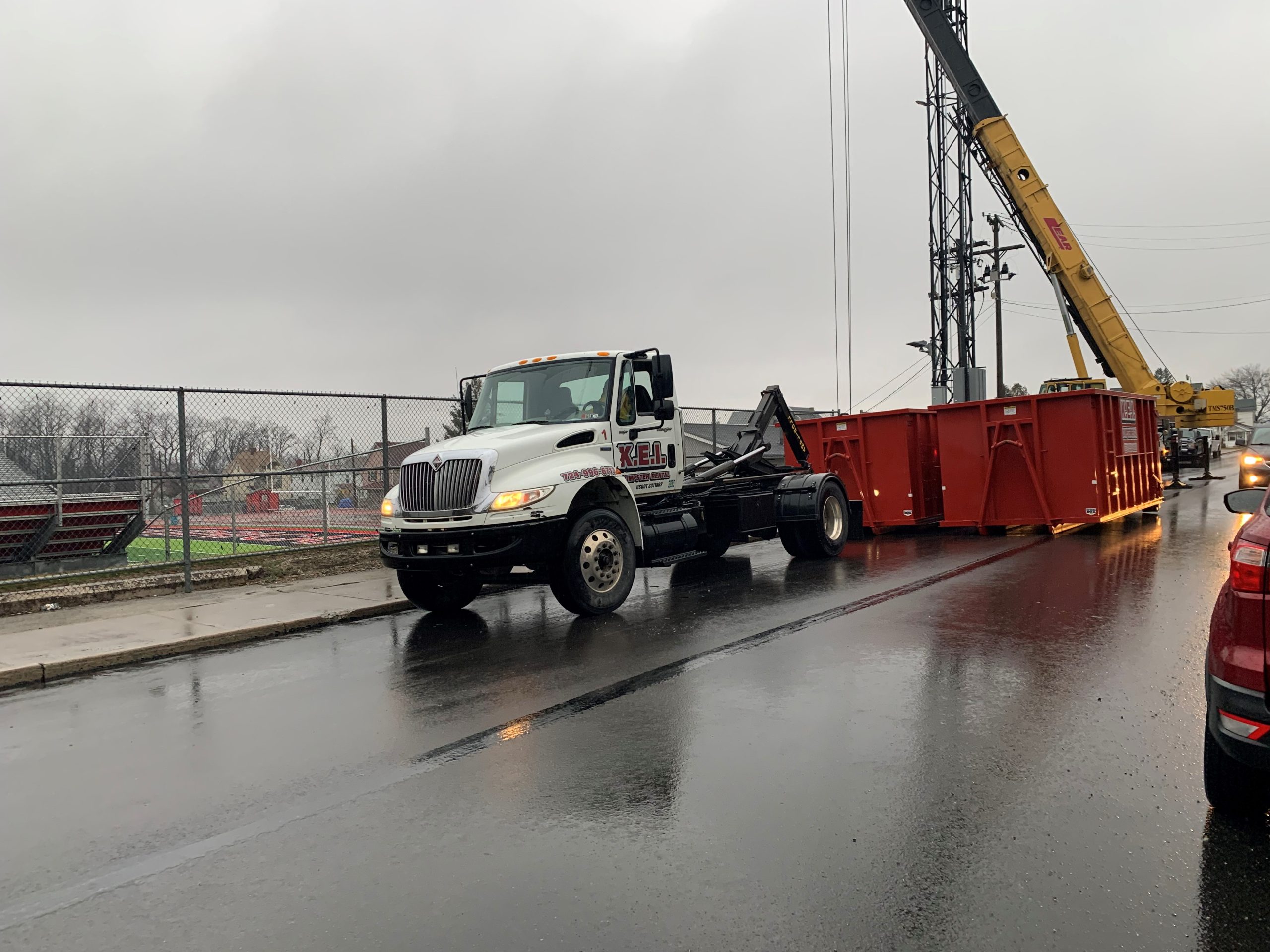 A KEI Dumpster Rental truck delivers two construction dumpsters to a project site.
