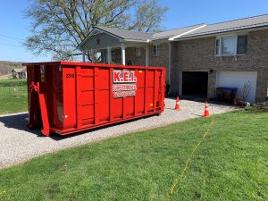 A red KEI roll-off dumpster sits in front of a home that needed local dumpster rentals for a home project.