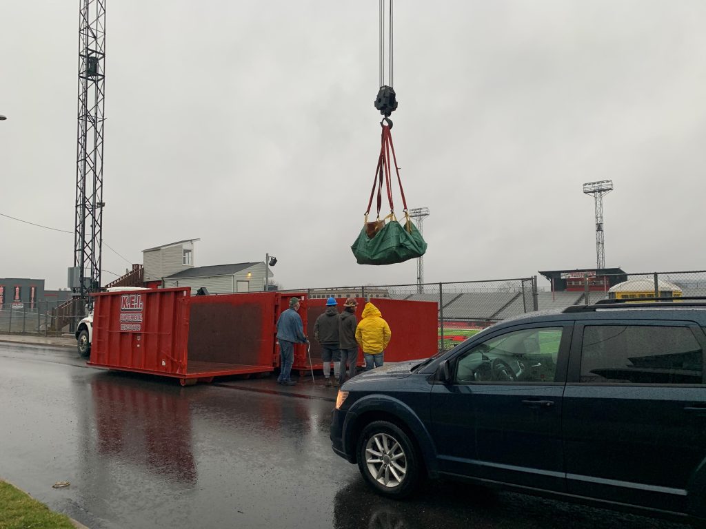 A KEI commercial dumpster rental is loaded at a construction site using a crane. 