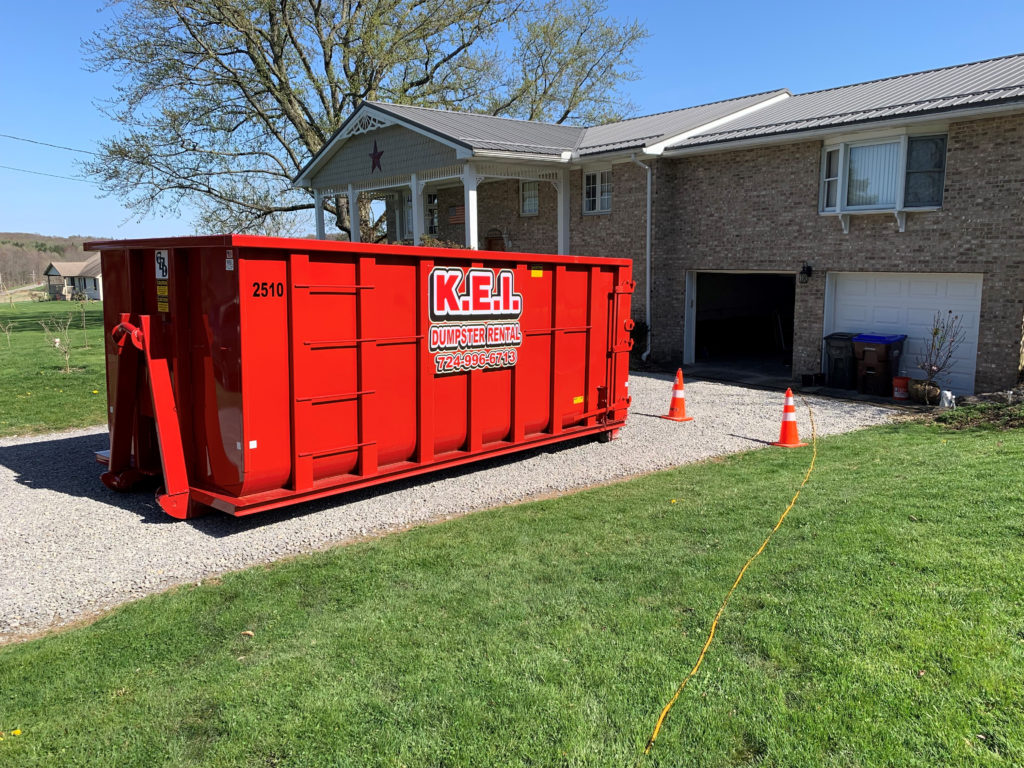 A red KEI dumpster rental sits in the driveway of a home. 